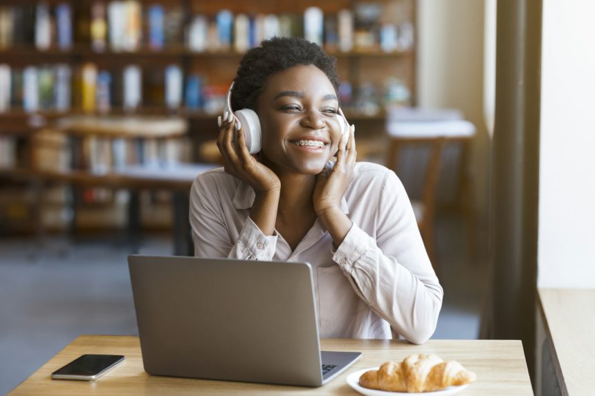 Black woman listening to music with headset, laptop in cafe